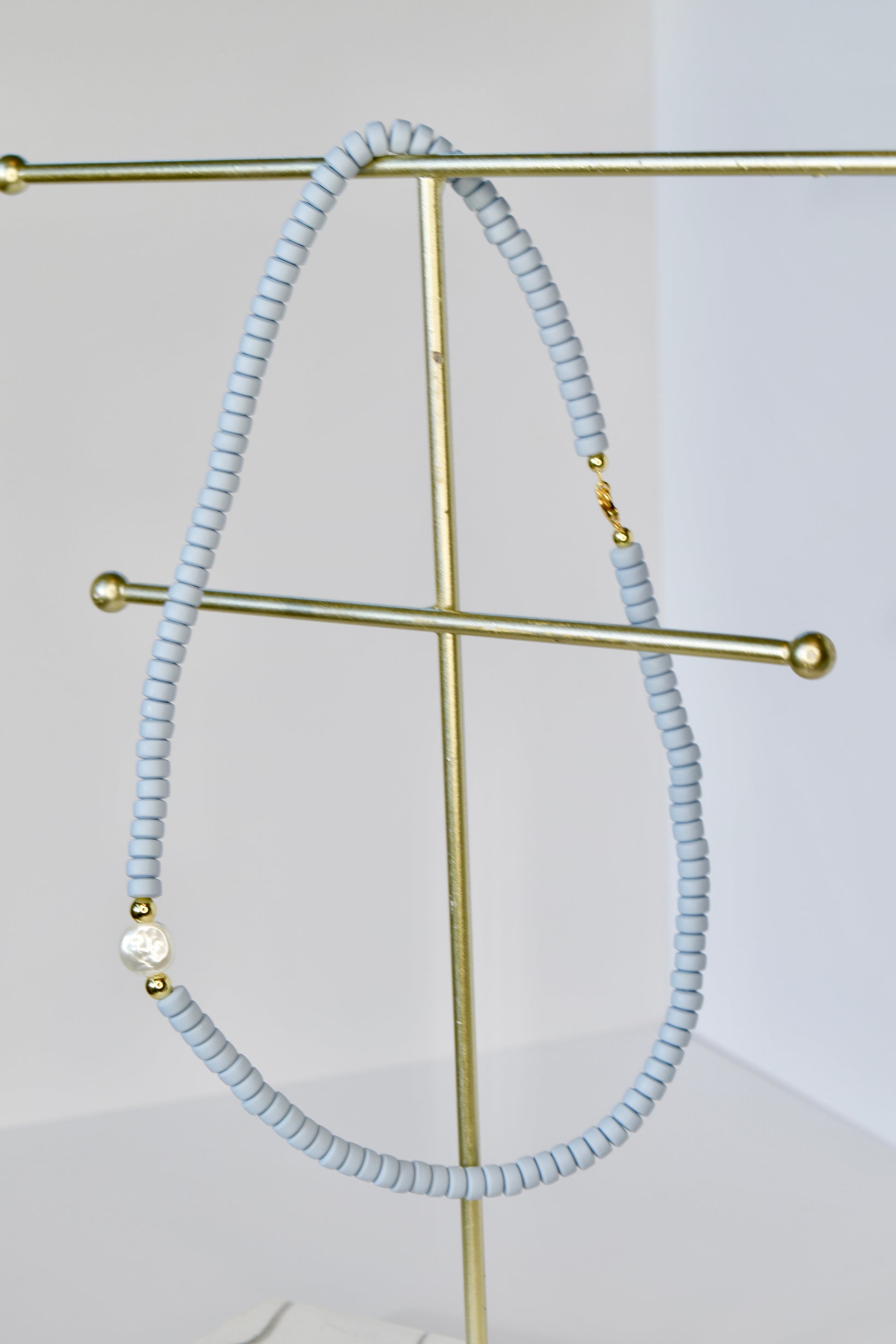 Light blue beaded necklace on a gold stand against a white background